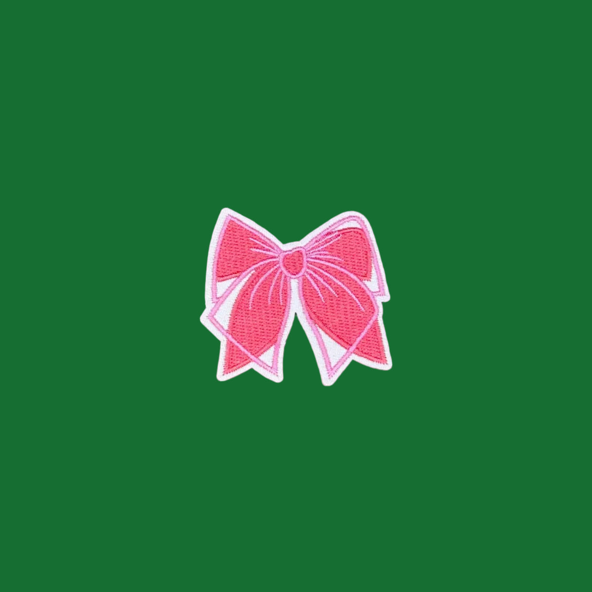 A pink embroidered bow patch with a white border, centered on a solid brown background.