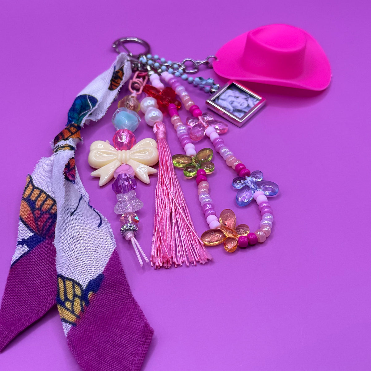 Detail of the 1-of-1 Pink Cowboy Hat Dolly Parton butterfly bag charm by PrettyMUCH, with cream bow strand and acrylic butterfly beads.