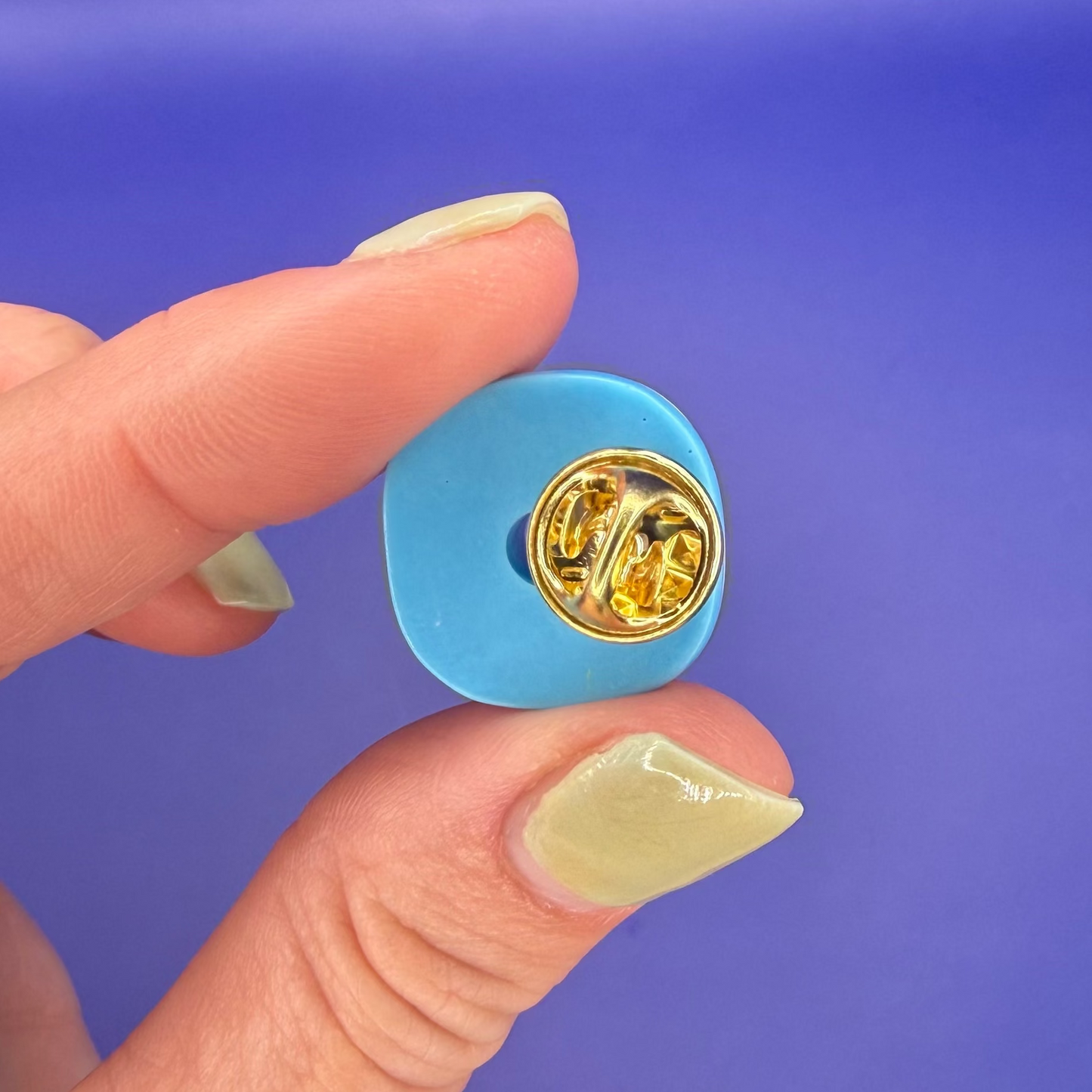 Back of the pastel glazed donut enamel pin showing the gold clutch back, held in hand