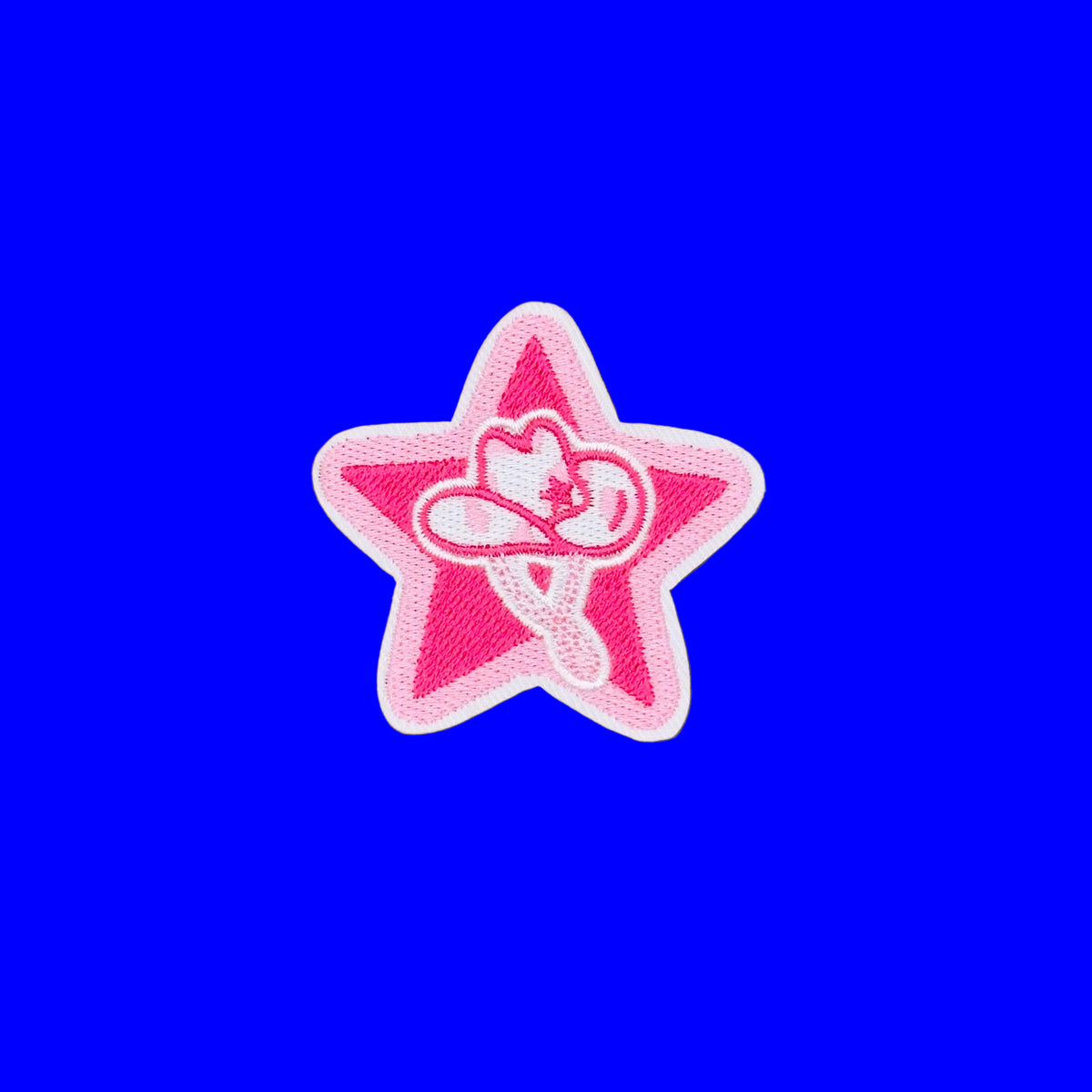 A pink embroidered star-shaped patch with a white border and a central white heart-and-star motif, placed on a smooth brown background.