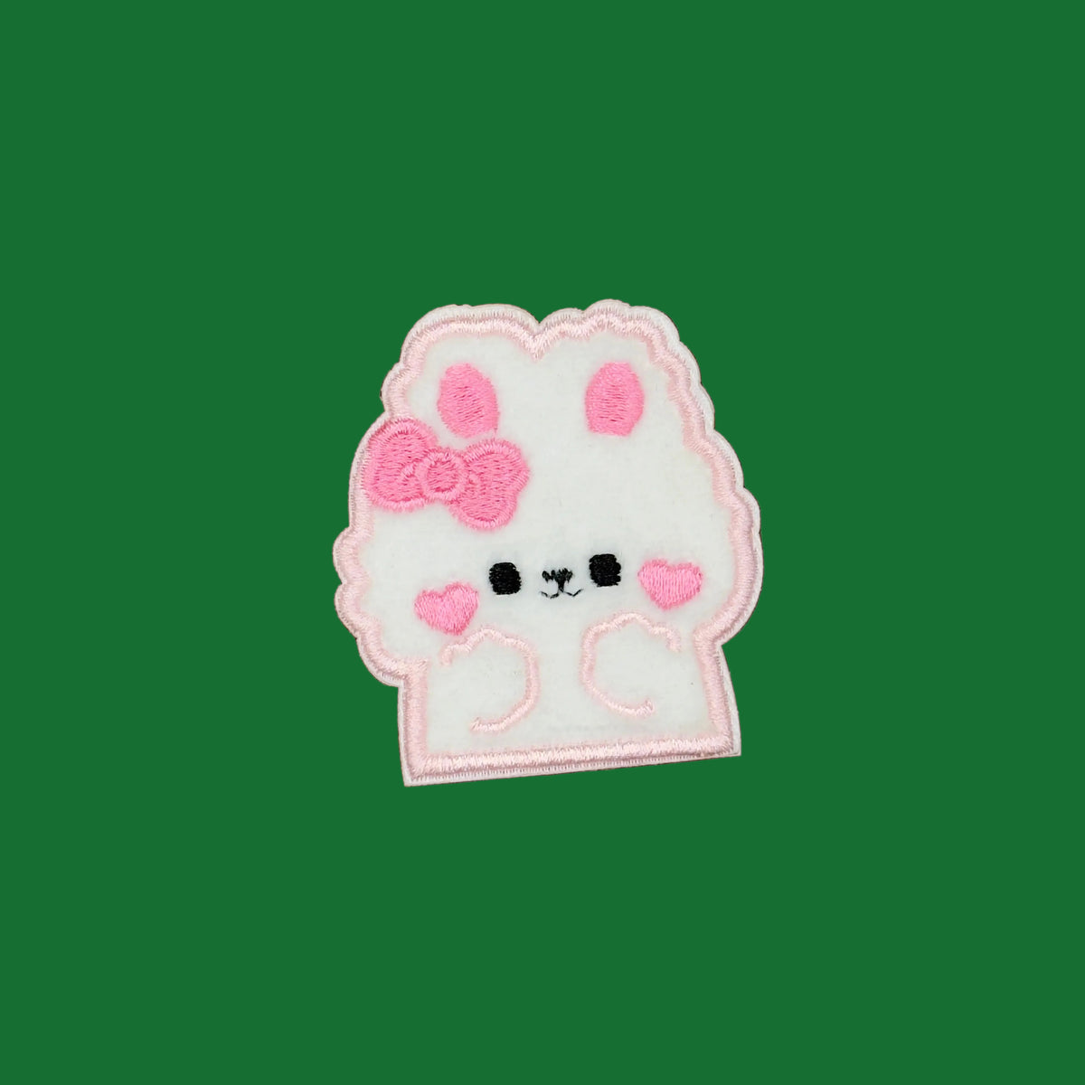 A white embroidered bunny patch with pink details, including a bow, ears, hearts, and facial features, shown on a solid brown background.
