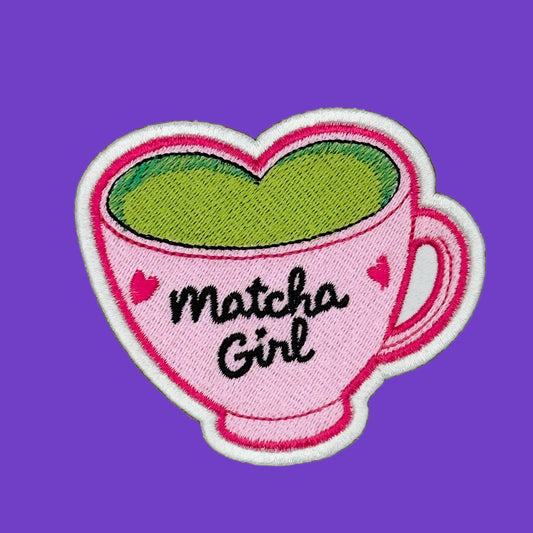 Matcha Girl written on a pink heart-shaped matcha latte cup with small pink hearts on the side of the Matcha Girl logo. Embroidered iron-on patch in a large size on a solid purple background.