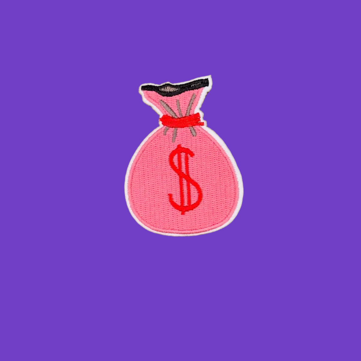 An embroidered patch shaped like a pink money bag with a red dollar sign, black top, and red drawstring, shown on a solid brown background.