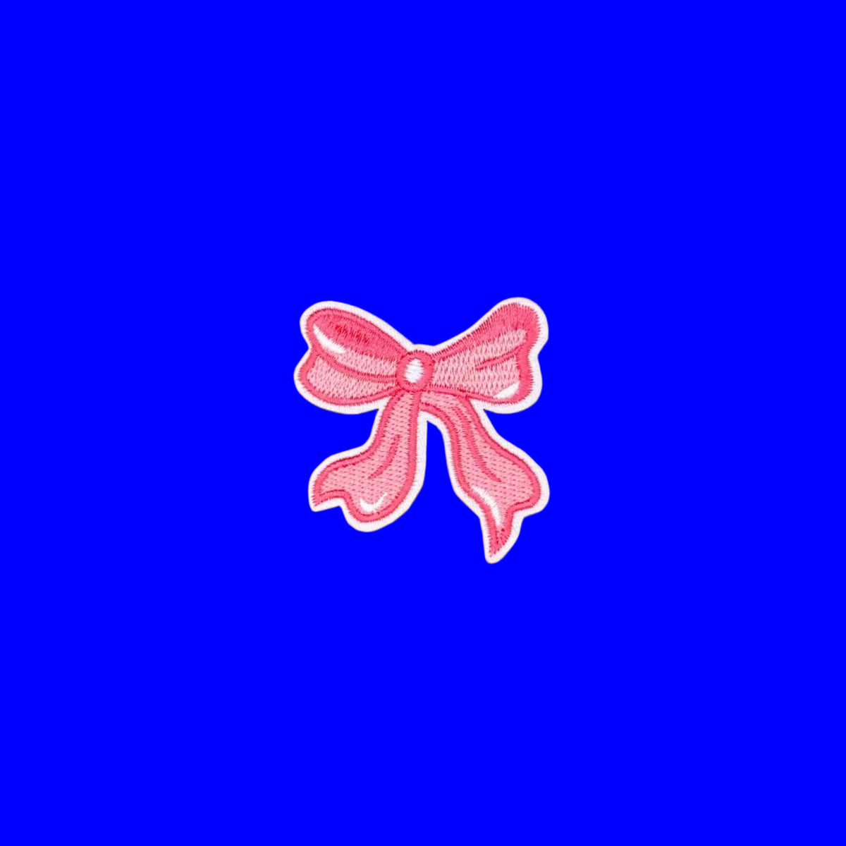 A pink embroidered bow patch with a white border, centered on a smooth brown background.