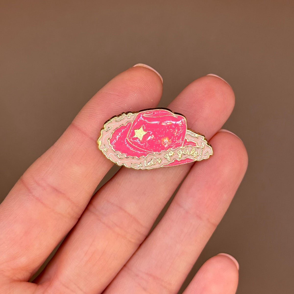 Let's Go Girls pink cowboy hat enamel pin held in hand
