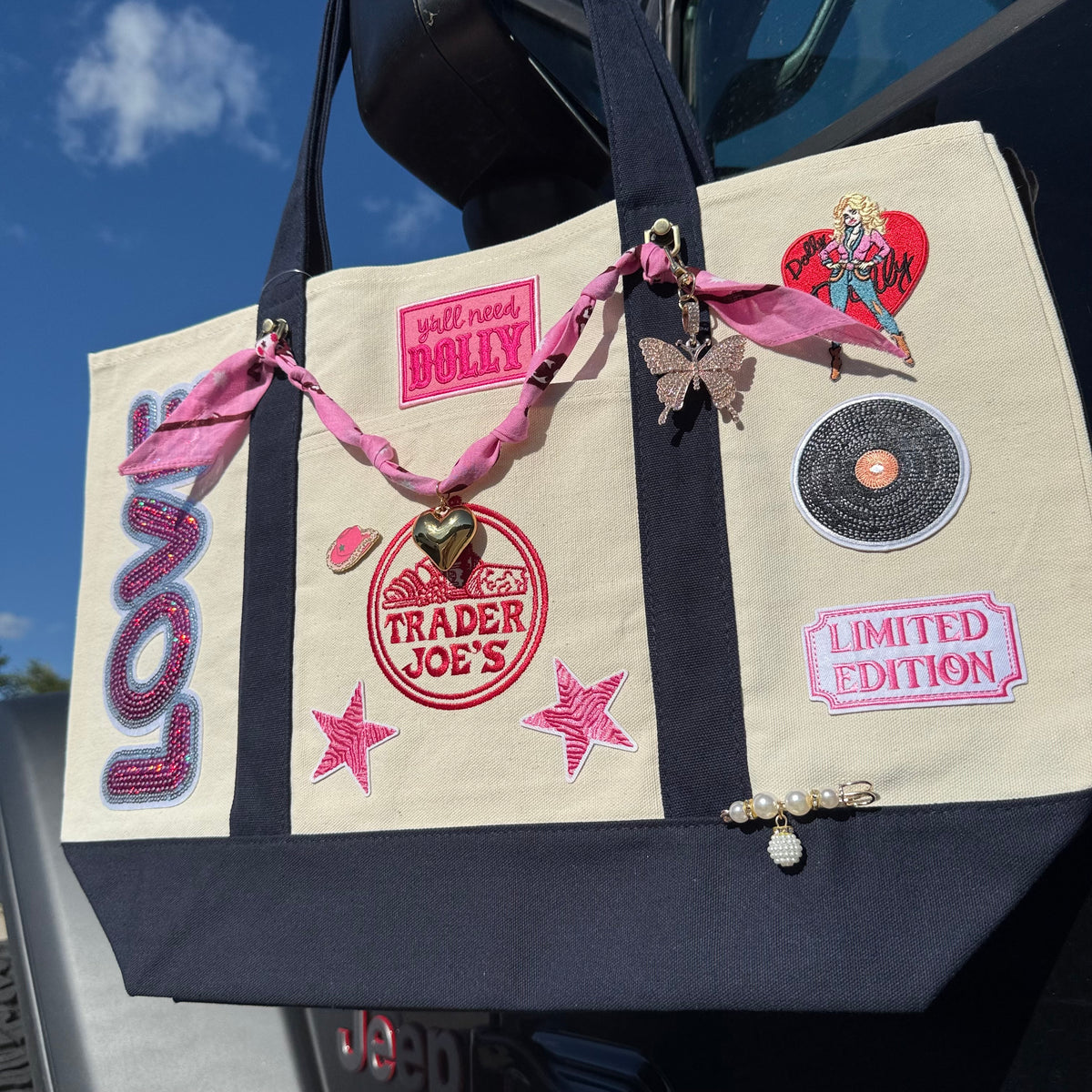 Angled view of the Dolly Parton Limited Edition large tote with the red heart Dolly patch, LIMITED EDITION patch, pink zebra stars and pearl drop bar pin