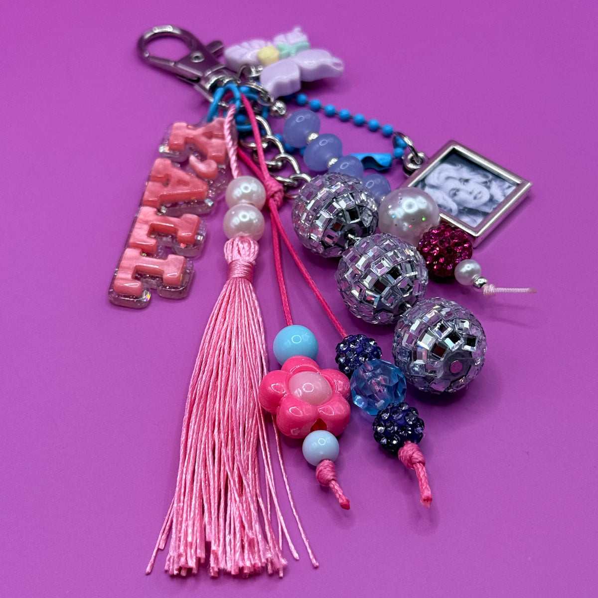 Close-up of the 1-of-1 Y'all Disco Dolly bag charm by PrettyMUCH with a framed portrait charm on a sky-blue ball chain.