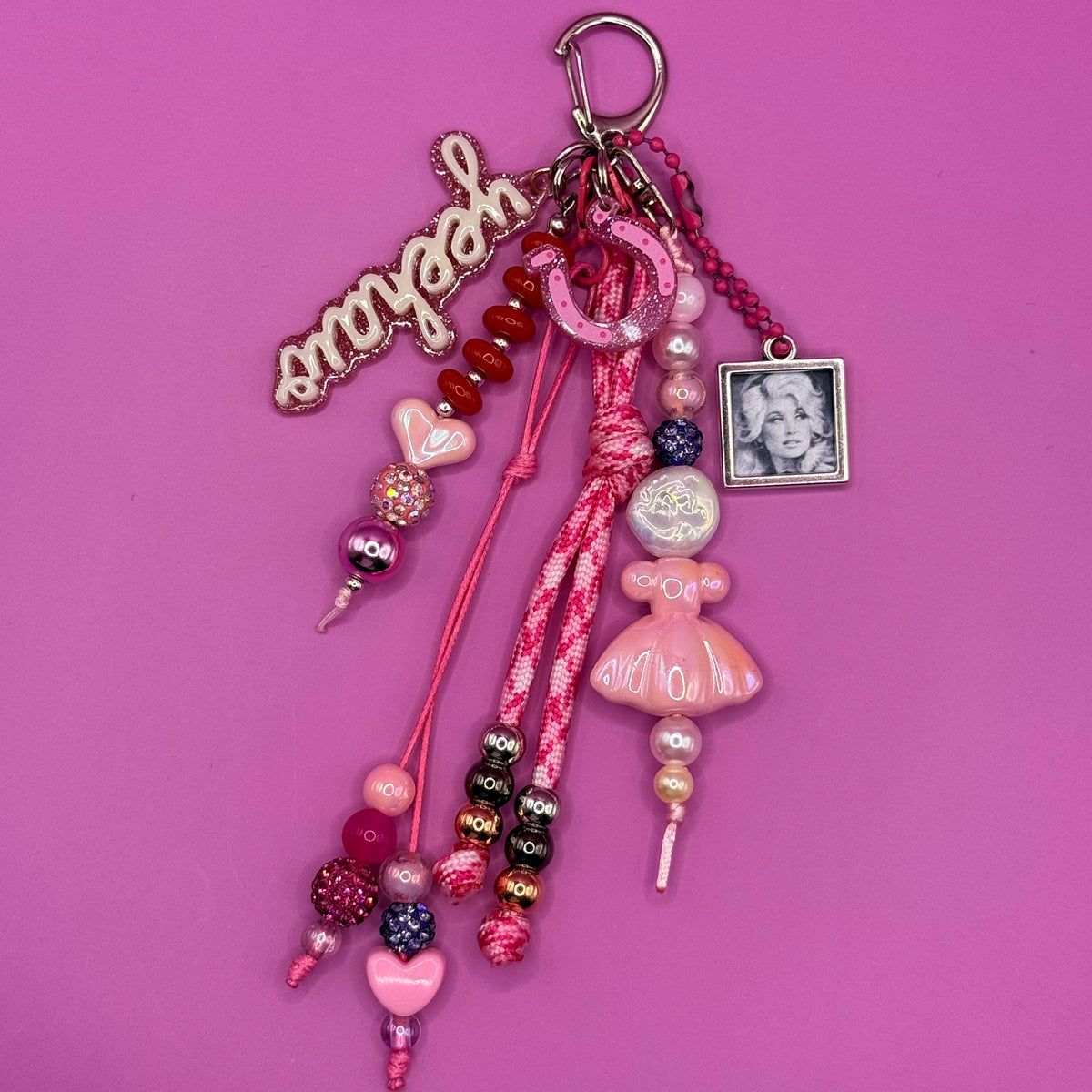 1-of-1 handmade Dolly trinket bag charm with a glittery pink howdy charm, pink horseshoe, braided pink paracord, pearl and heart beads and a framed portrait charm on a silver clasp.