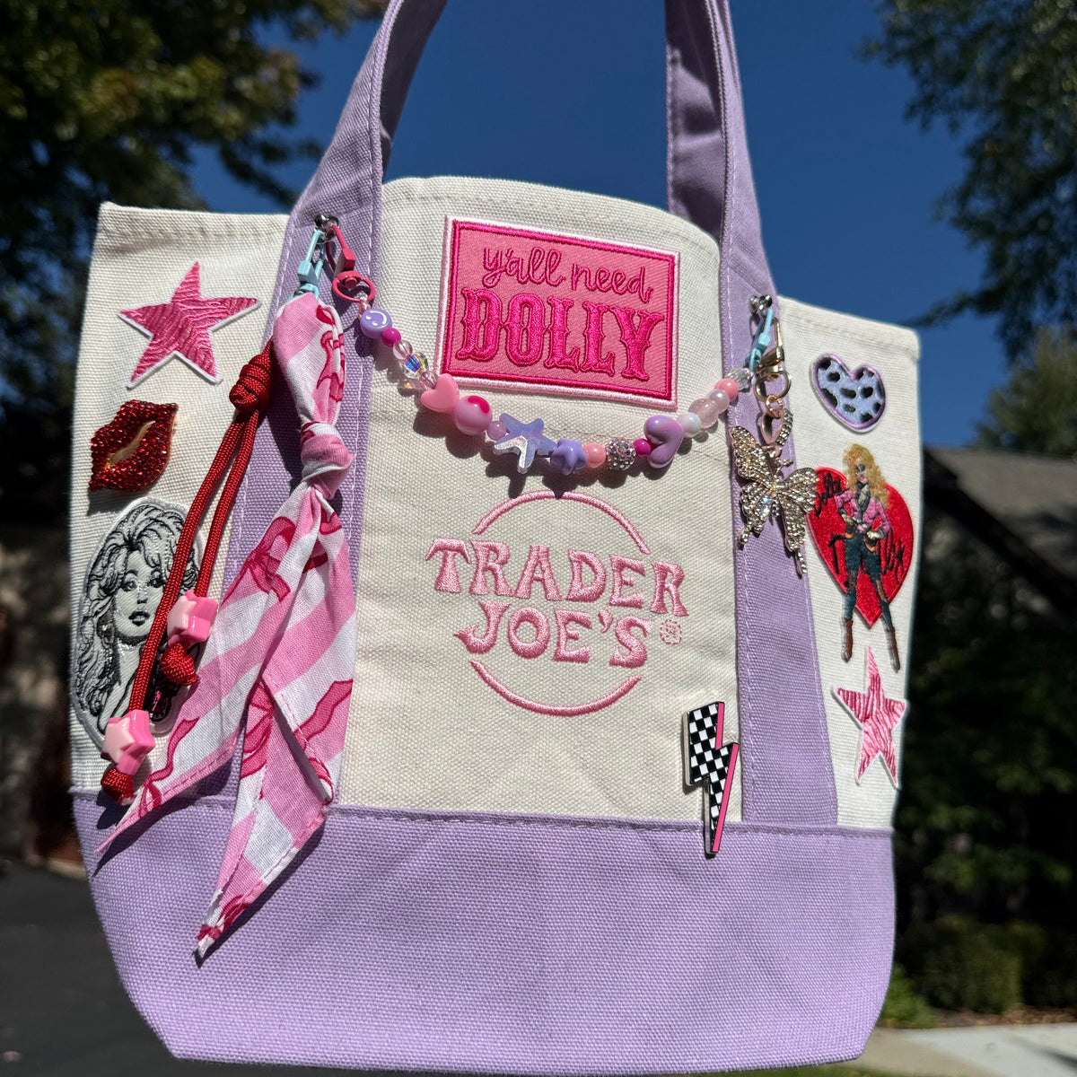 Dolly Parton Pretty in Pastel mini tote by PrettyMUCH, a lavender and cream Trader Joe's canvas tote with Dolly patches and charms.