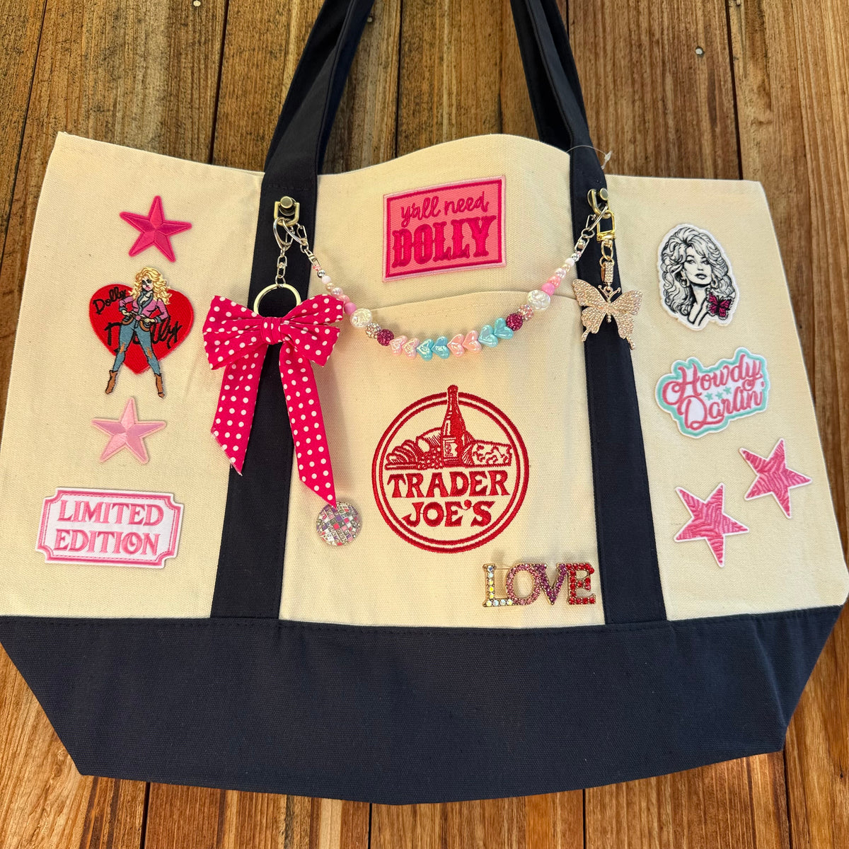 Dolly Parton Big Love large tote by PrettyMUCH, a natural and navy Trader Joe's canvas tote with all three Dolly patches, a beaded bag chain and a hot pink polka-dot bow.