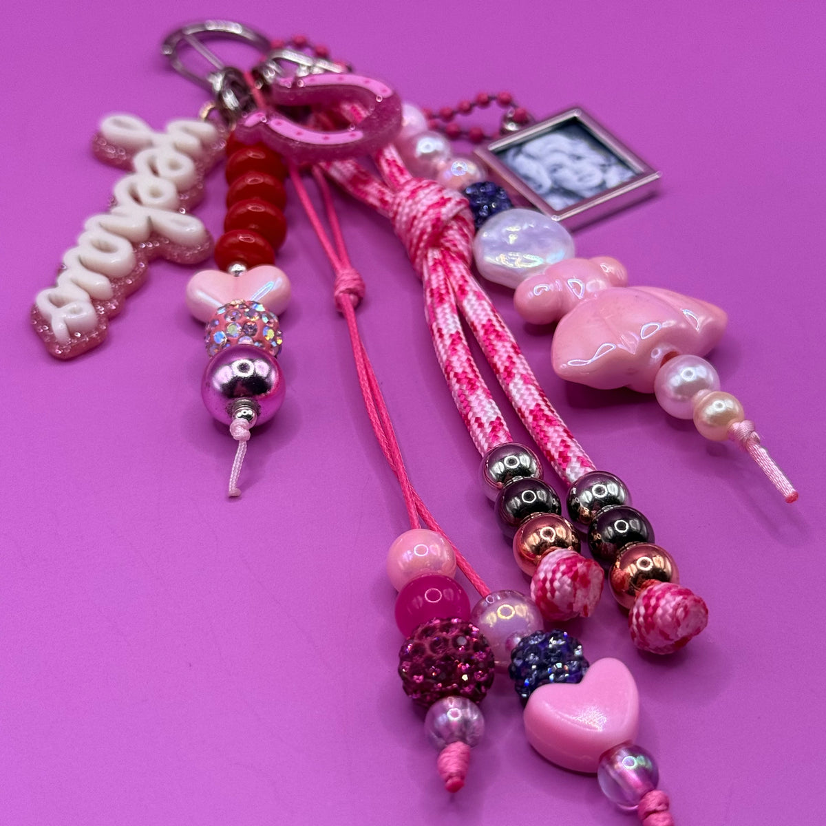 Detail of the 1-of-1 Howdy Horseshoe Dolly bag charm by PrettyMUCH, with pink horseshoe, rhinestones and a pink ball chain portrait charm.