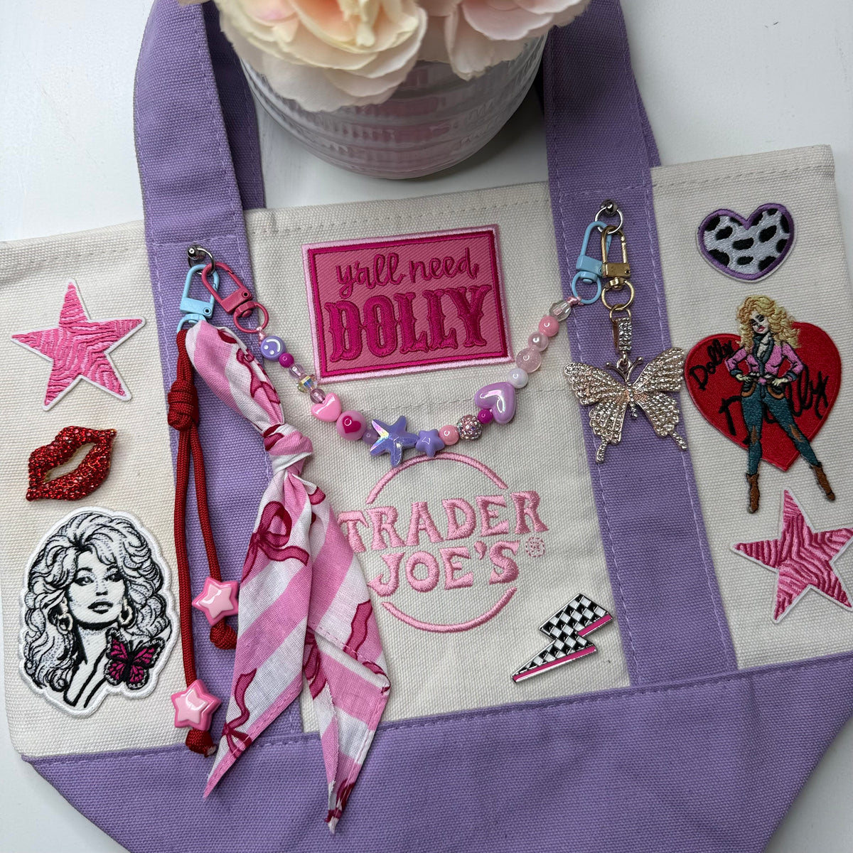 Dolly Parton Pretty in Pastel mini tote by PrettyMUCH, a lavender and cream Trader Joe's canvas tote with Dolly patches and charms.