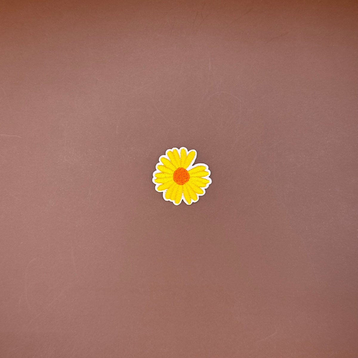 Yellow daisy embroidered iron-on patch with a burnt orange center