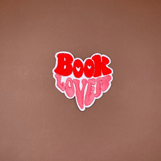 Book lover iron-on patch with red and pink bubble letters stacked into a heart shape
