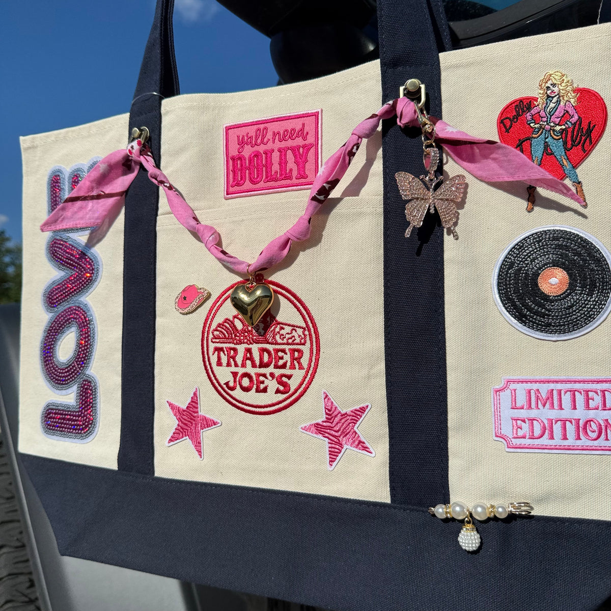 Dolly Parton Limited Edition large tote showing the Dolly heart portrait patch, vinyl record patch, LIMITED EDITION patch and gold pearl and rhinestone bar pin
