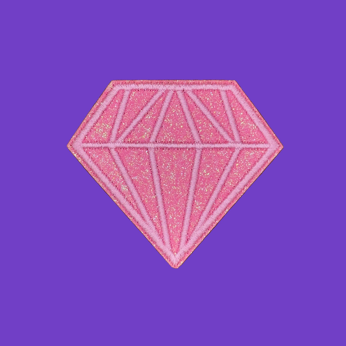 A pink glitter diamond-shaped patch with white embroidered lines forming a faceted gemstone pattern, shown on a solid brown background.