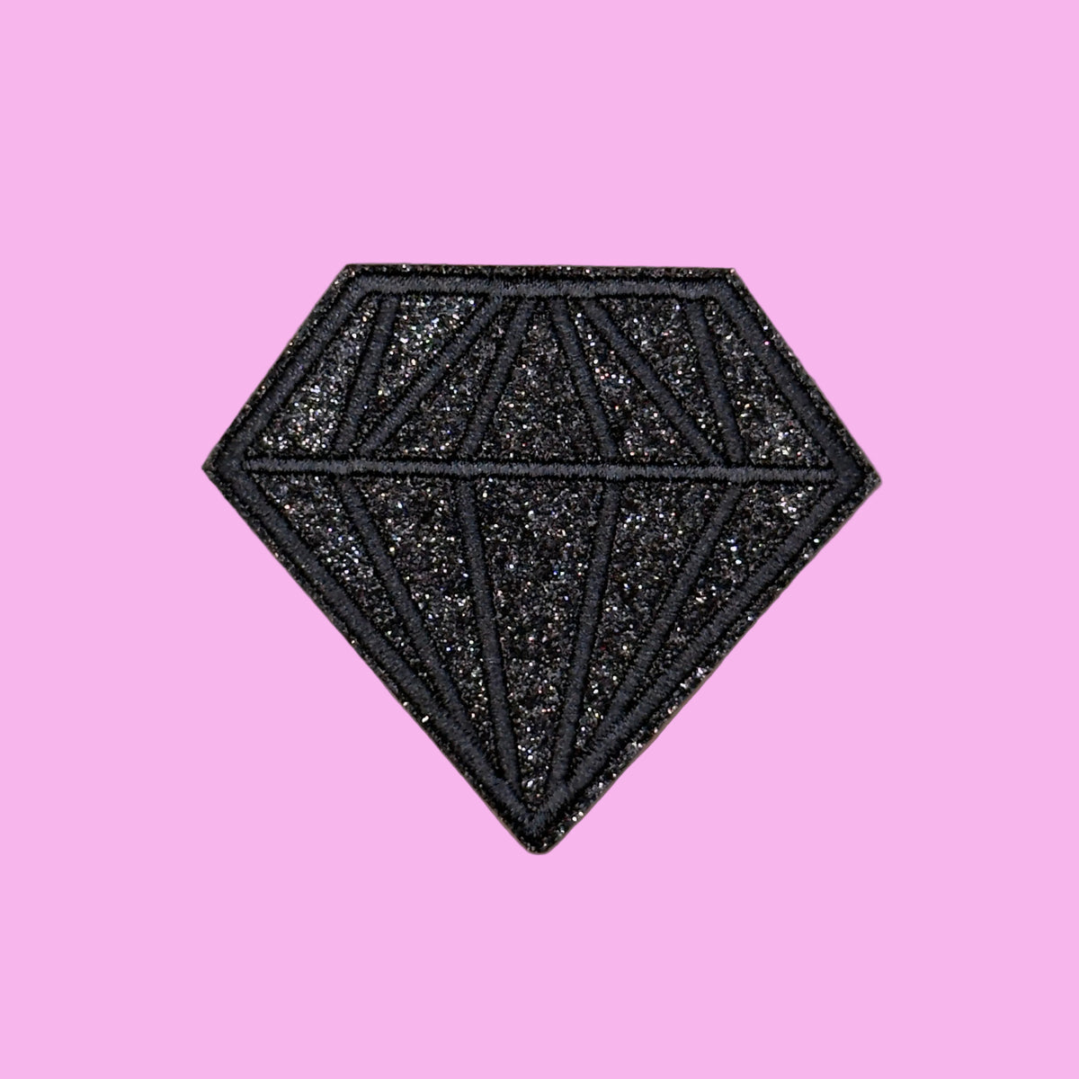 A black glitter diamond-shaped patch with geometric line details, centered on a solid dusty rose background.