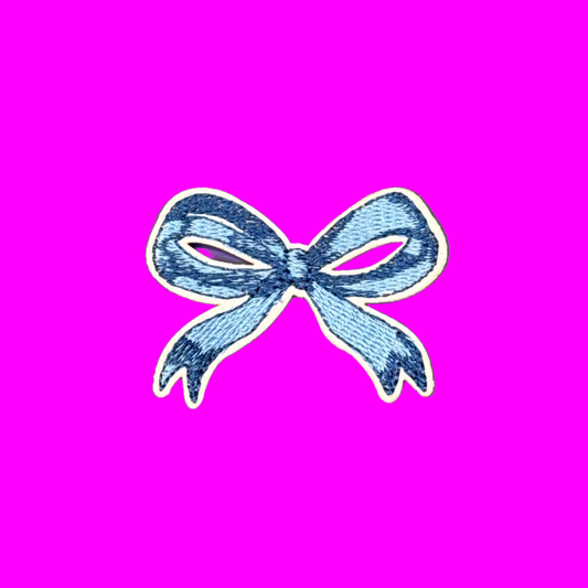 A small embroidered bow patch in shades of blue with a white border, centered on a solid purple background.