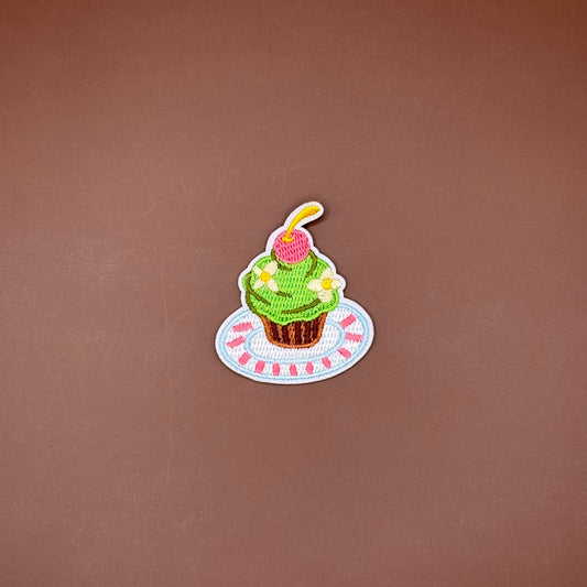 Iron-on patch of a cupcake with green swirled frosting and a cherry on a striped plate