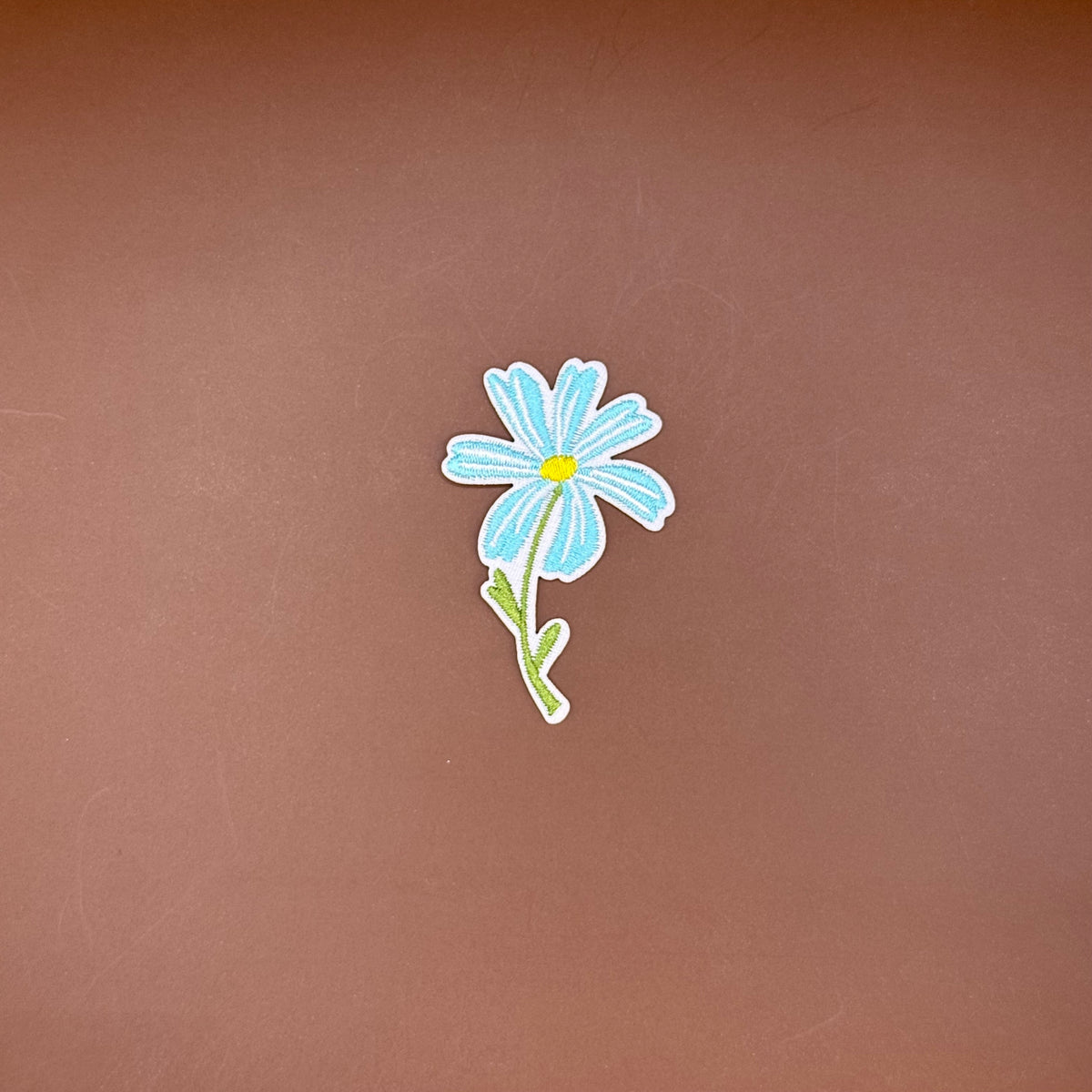 Sky blue daisy embroidered iron-on patch on its stem