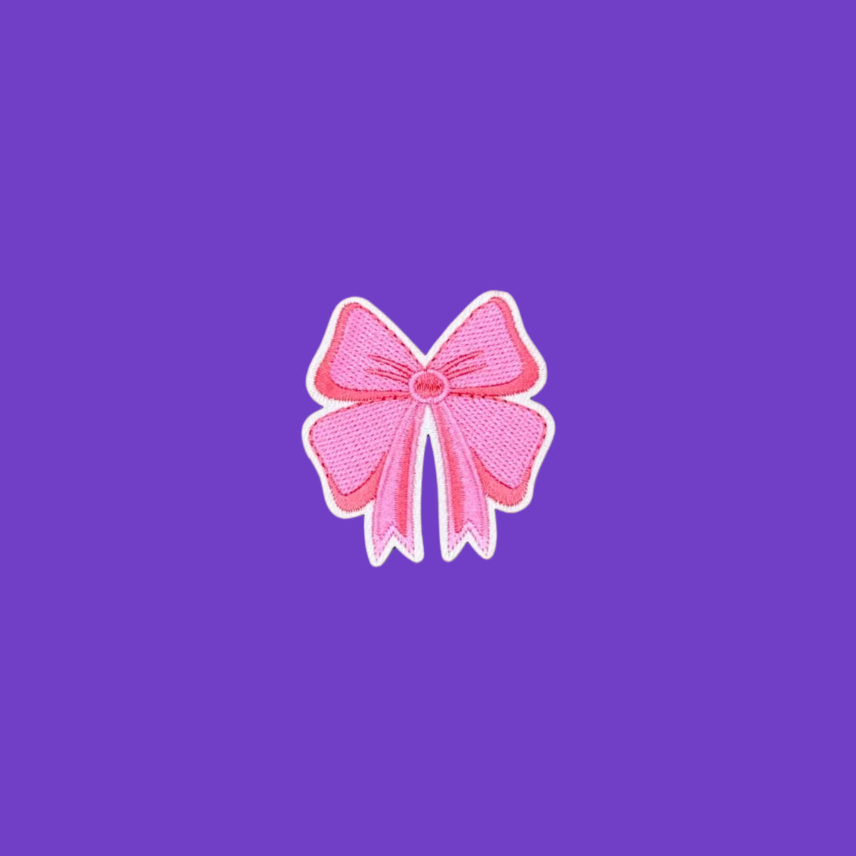 A pink embroidered bow patch with a white border, centered on a smooth brown background.