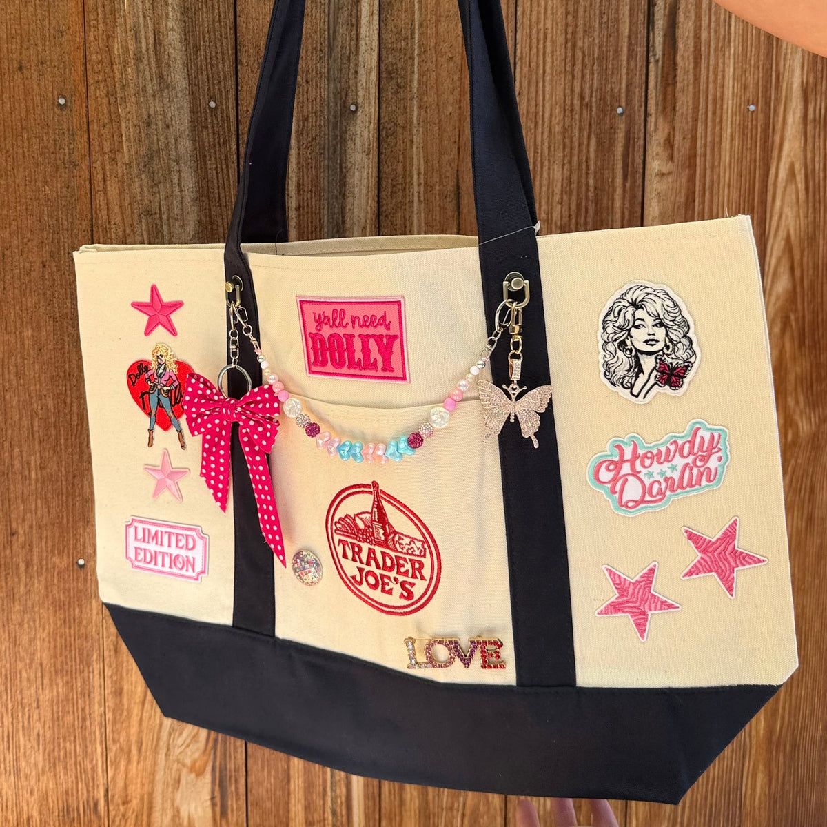 Dolly Parton Big Love large tote by PrettyMUCH, a natural and navy Trader Joe's canvas tote with all three Dolly patches, a beaded bag chain and a hot pink polka-dot bow.