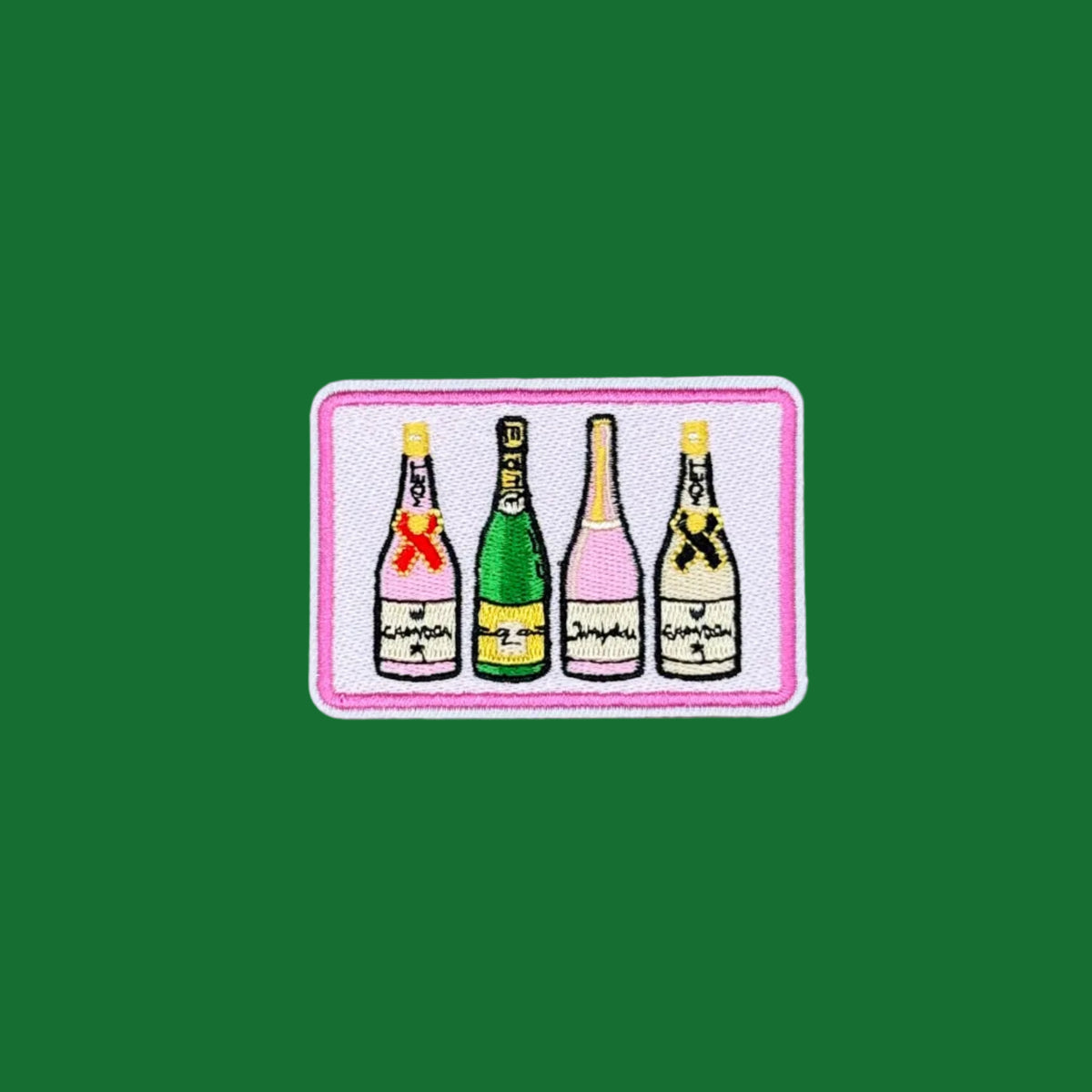 A rectangular embroidered patch featuring four champagne bottles in different colors (green, pink, yellow, black) on a white background with a pink border, displayed on a solid green surface.