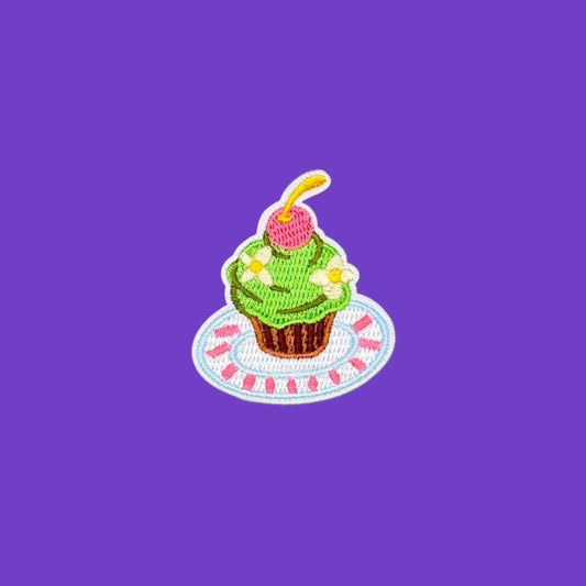 Iron-on patch of a cupcake with green swirled frosting and a cherry on a striped plate