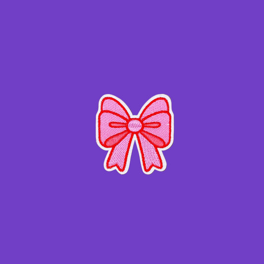A pink embroidered bow patch with a white border, centered on a smooth purple background.