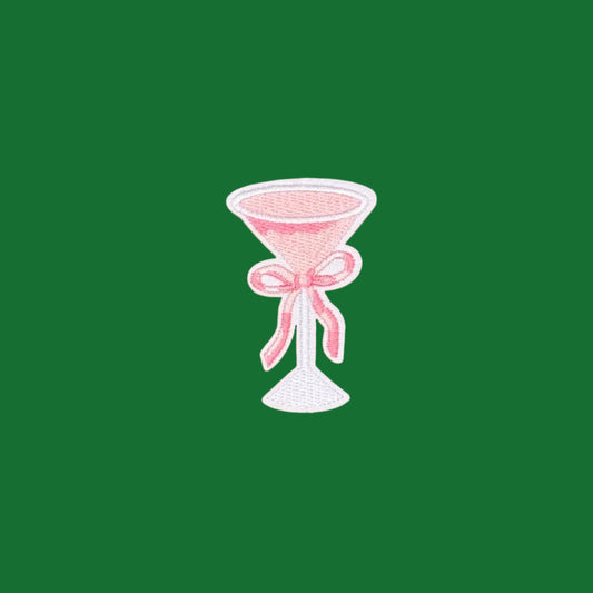 An embroidered patch of a pink cocktail glass tied with a pink ribbon.