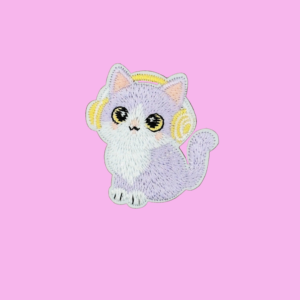 A cute embroidered patch of a lavender and white cat wearing yellow headphones, placed on a solid brown background.