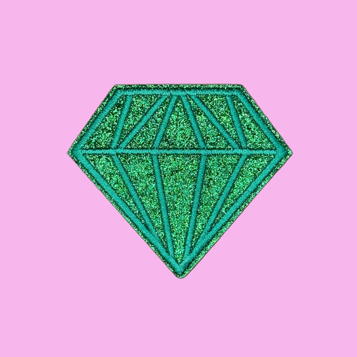 A green glitter diamond-shaped patch with a stitched geometric pattern, shown on a solid brown background.
