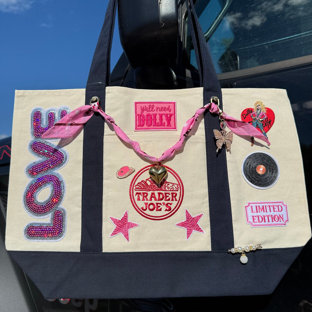 Straight-on front view of the Dolly Parton large custom tote with sequin LOVE patch, y'all need DOLLY patch, pink bandana bag chain with gold heart and rhinestone butterfly charm
