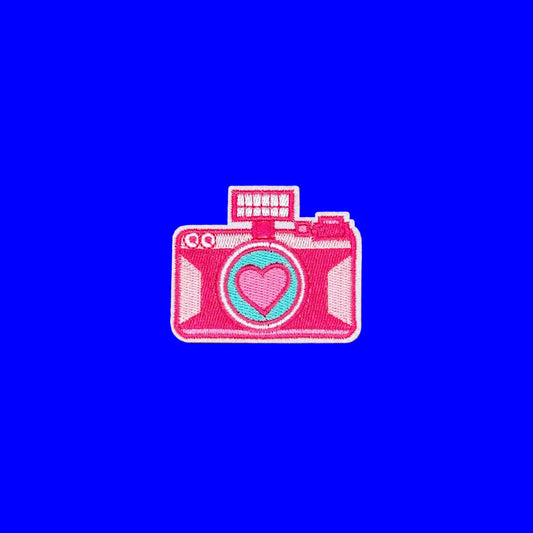 Hot pink camera iron-on patch with a heart-shaped lens and a flash cube on top