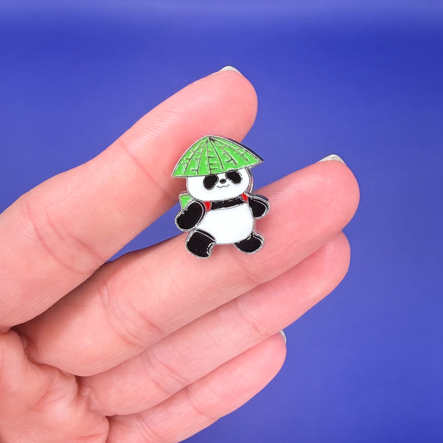Panda enamel pin wearing a green leaf hat and a backpack with red straps