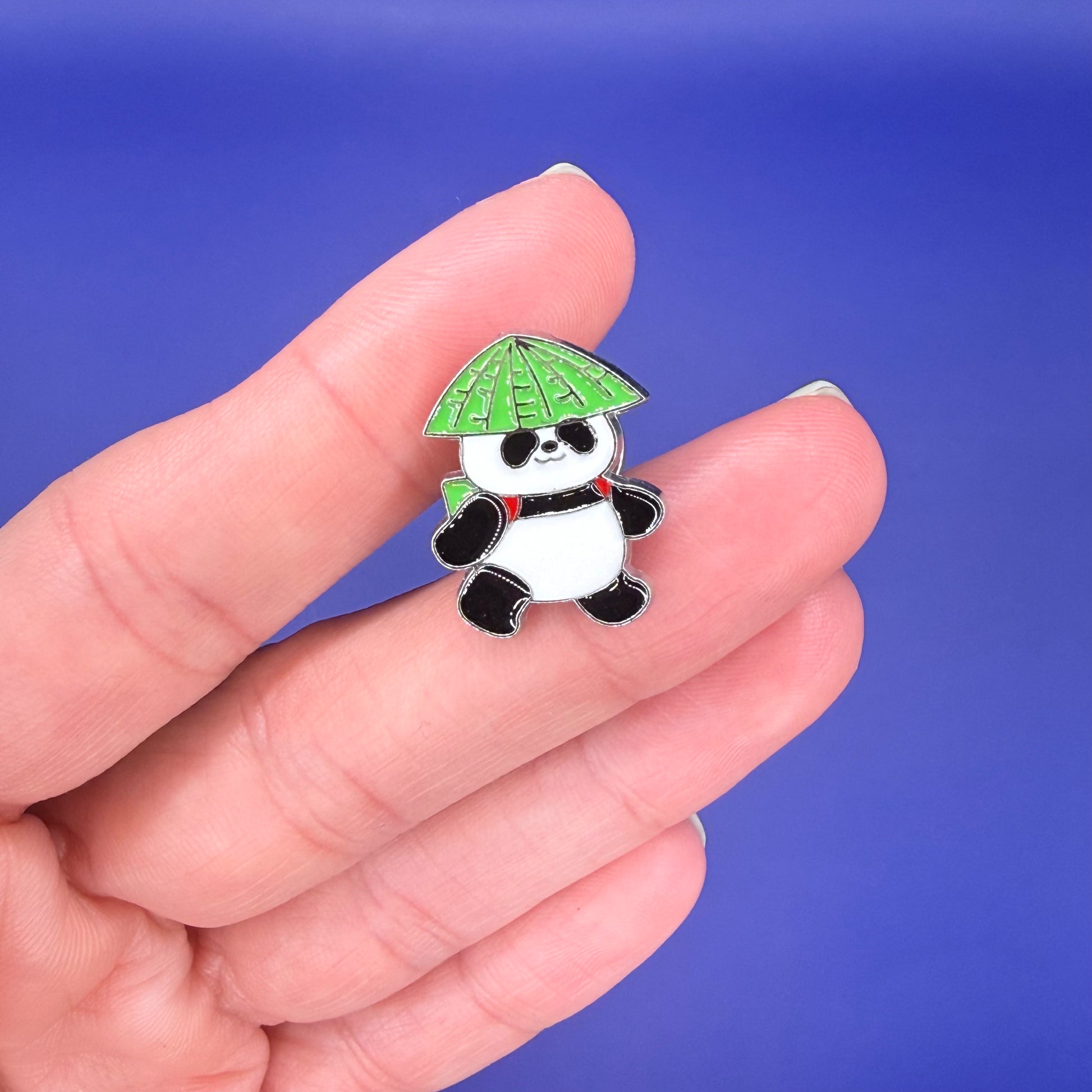 Panda enamel pin wearing a green leaf hat and a backpack with red straps