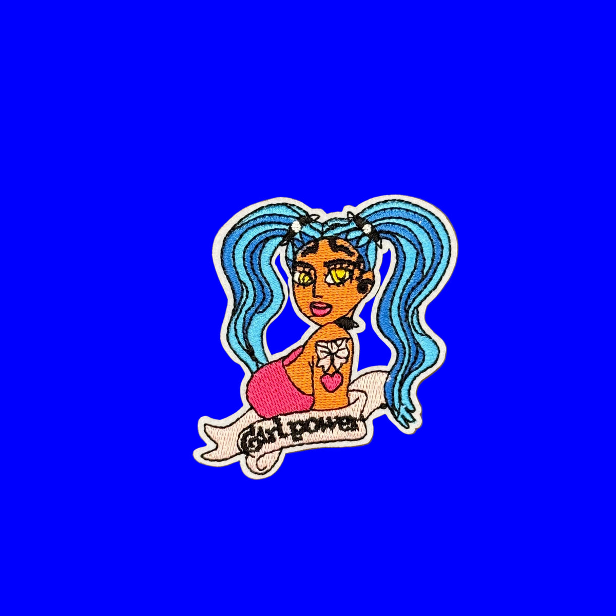Female cartoon character with hair in blue pig tails and 'Girl Power' written underneath like a vintage tattoo. Embroidered, iron-on patch on a blue background.