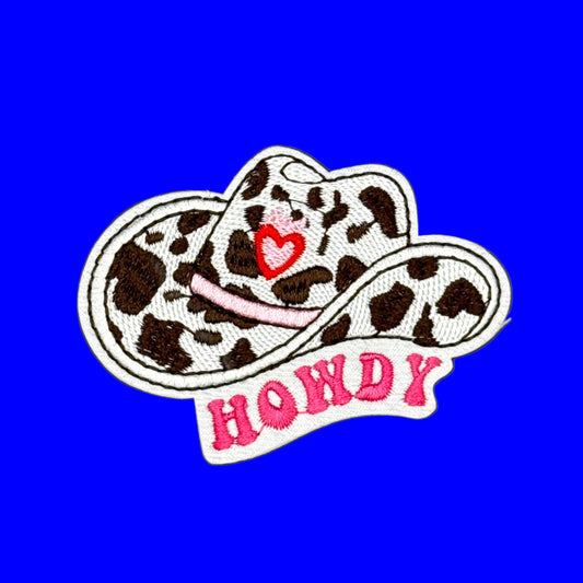 An embroidered patch featuring a cowboy hat with a brown and white leopard print, a pink heart on the brim, and the word 'HONDA' in pink letters on a white banner below, set against a solid blue background.