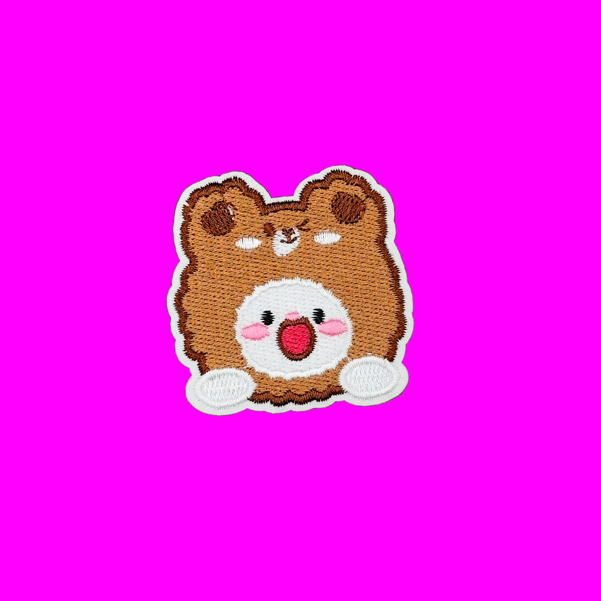 A cute embroidered patch of a smiling brown bear face with a white inner face, pink cheeks, and a red mouth, shown on a solid brown background.