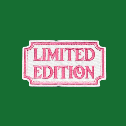 A rectangular embroidered patch with scalloped edges reading 'LIMITED EDITION' in pink lettering on a white background, set against a solid dark blue backdrop.