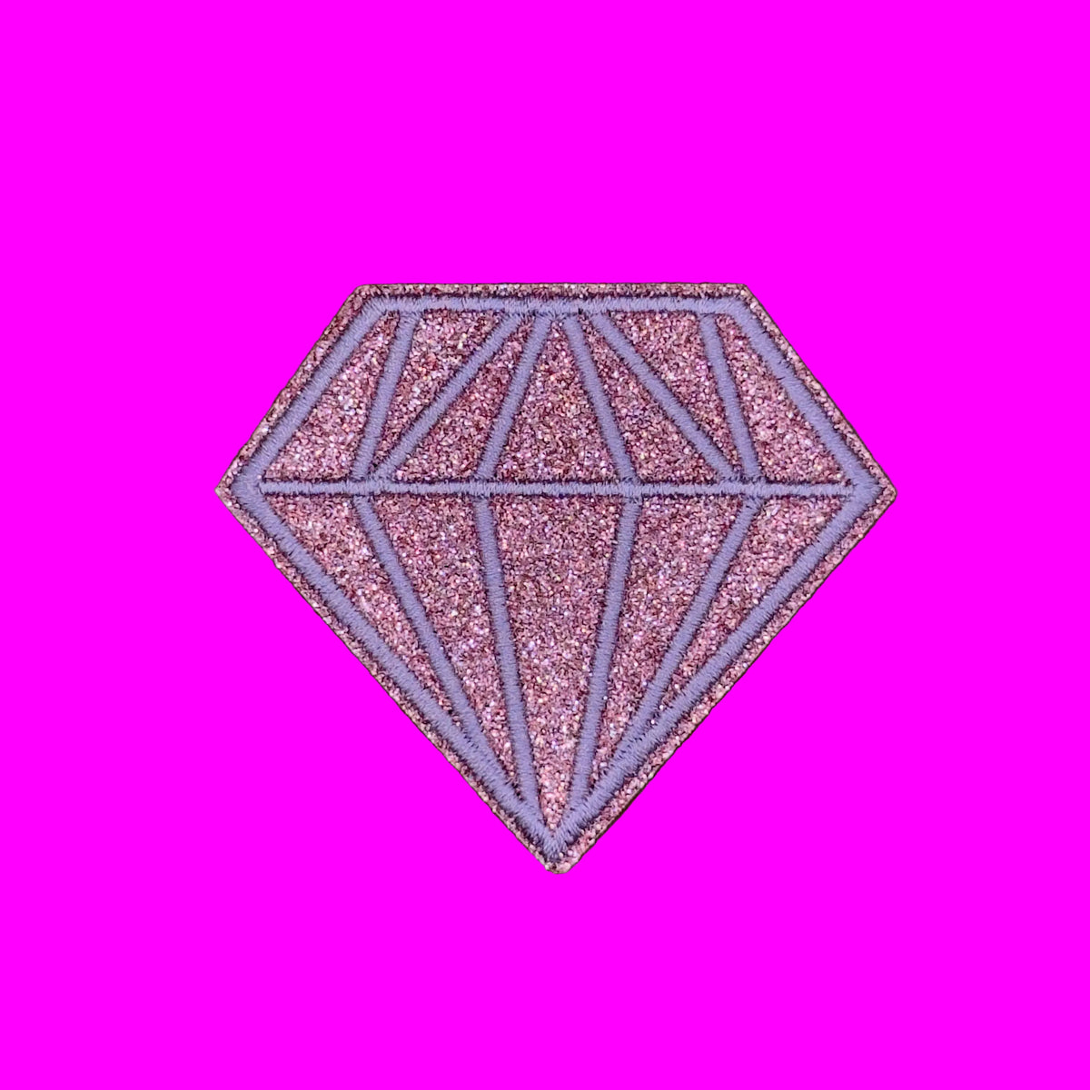 A glittery pink and purple diamond-shaped patch with geometric line details, shown on a solid brown background.