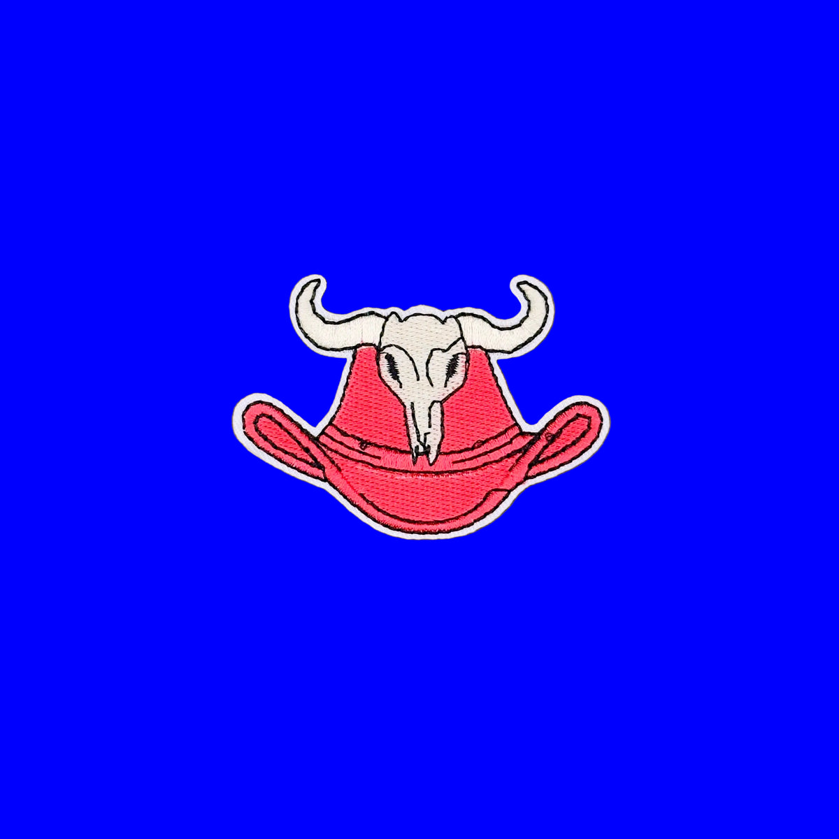 An embroidered patch featuring a white longhorn above a red cowboy hat, outlined in white, placed on a plain blue background.