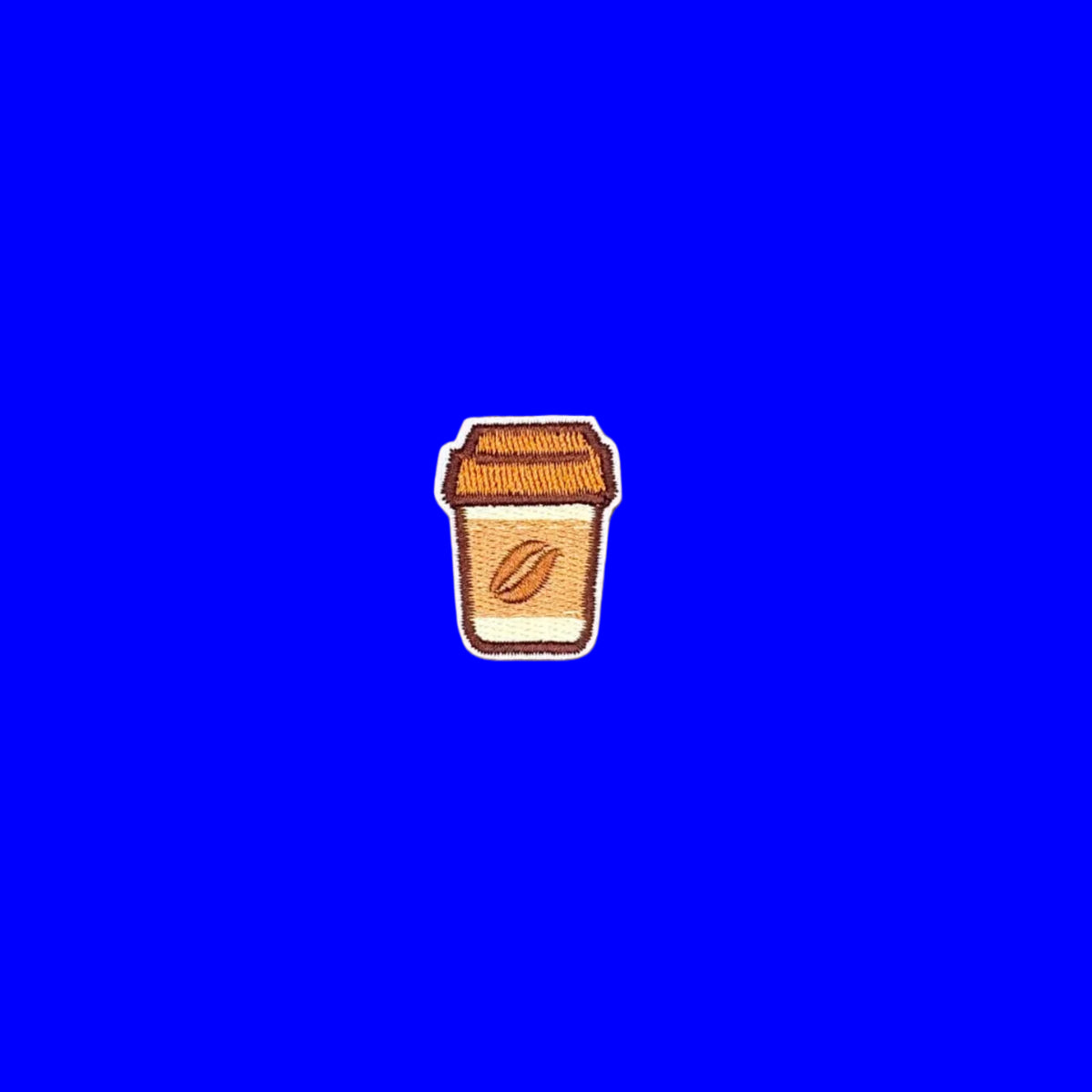 A small embroidered patch shaped like a takeaway coffee cup with a coffee bean detail, shown on a solid brown background.