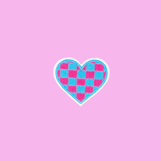 A heart-shaped patch featuring a pink and blue checkerboard pattern with a white border, centered on a pink background.