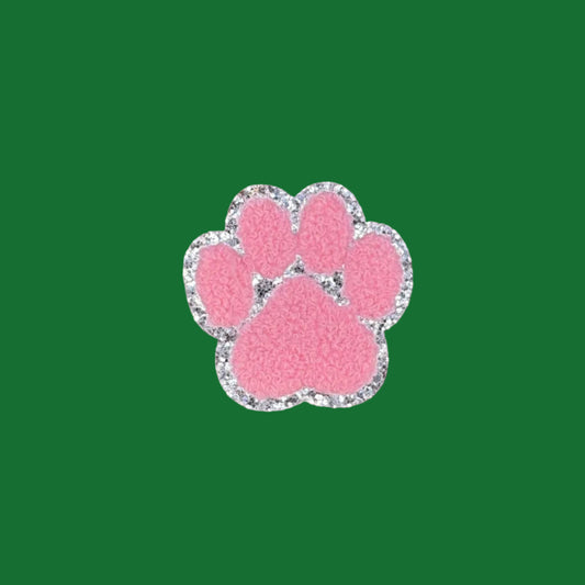 A pink paw print charm with a silver glitter border, centered on a brown textured background.