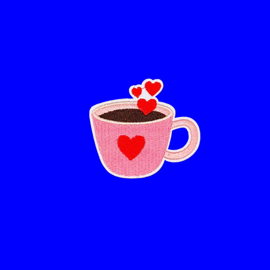A pink embroidered coffee mug patch with red hearts, shown on a solid blue background.