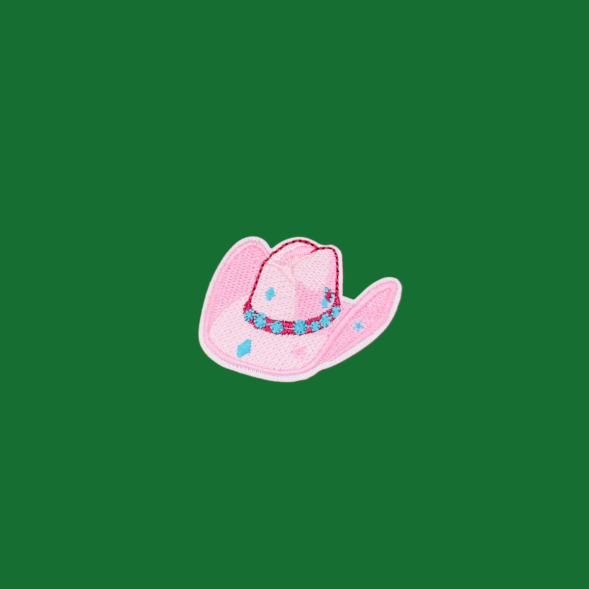 A pink embroidered cowboy hat patch with blue and red accents, placed on a solid green background.