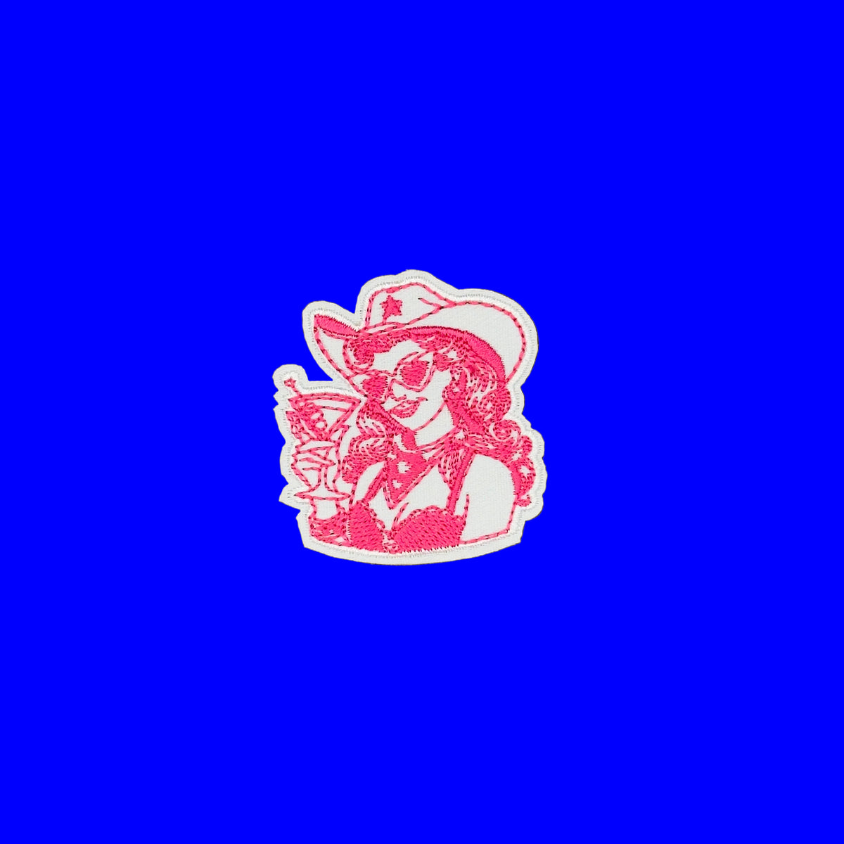 A small embroidered patch featuring a pink woman in a cowgirl outfit and hat holding a cocktail glass, outlined in white, placed on a solid blue background.