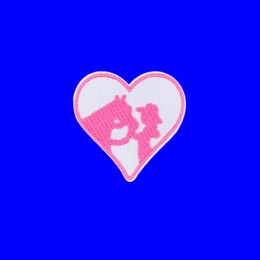 A heart-shaped embroidered patch featuring a pink silhouette of a horse and rider on a white background with a pink border, displayed on a solid blue surface.