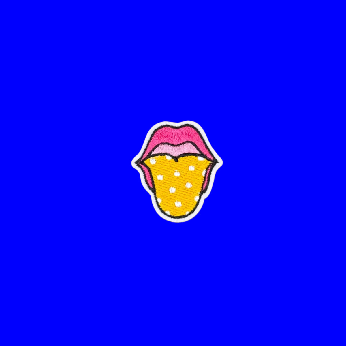 Pop Art pink lips with yellow dot tongue iron on patch on a blue solid background.